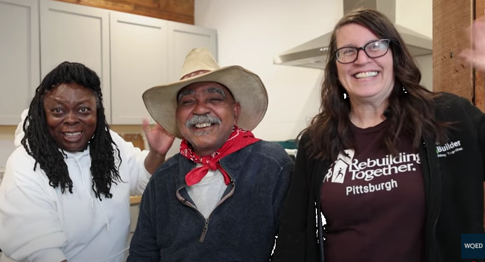 Still from the WQED video about Rebuilding Together Pittsburgh. The image features three people standing next to each other and smiling in a kitchen.